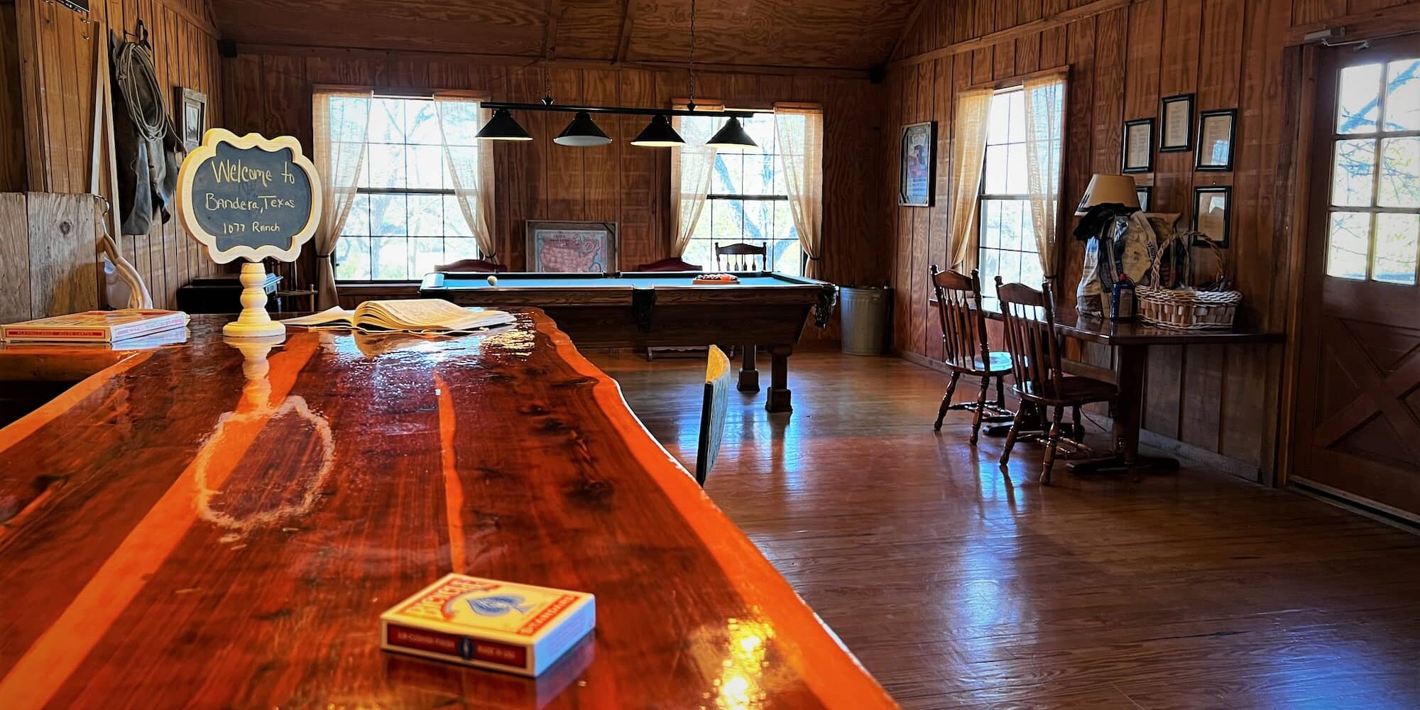 A pool table is viewed from across the room in the lodge lounge, a deck of cards sits on the bar in foreground.
