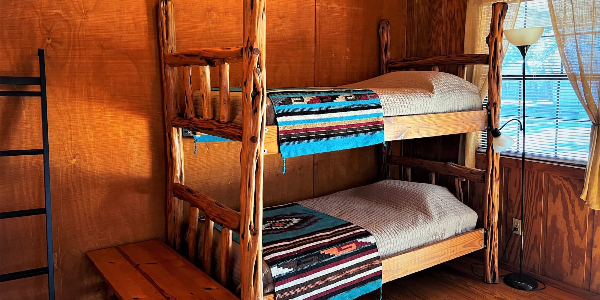 Bunkbeds in a guest cabin are fitted with bright turquoise western style bedding, a ladder sits propped against the wall.